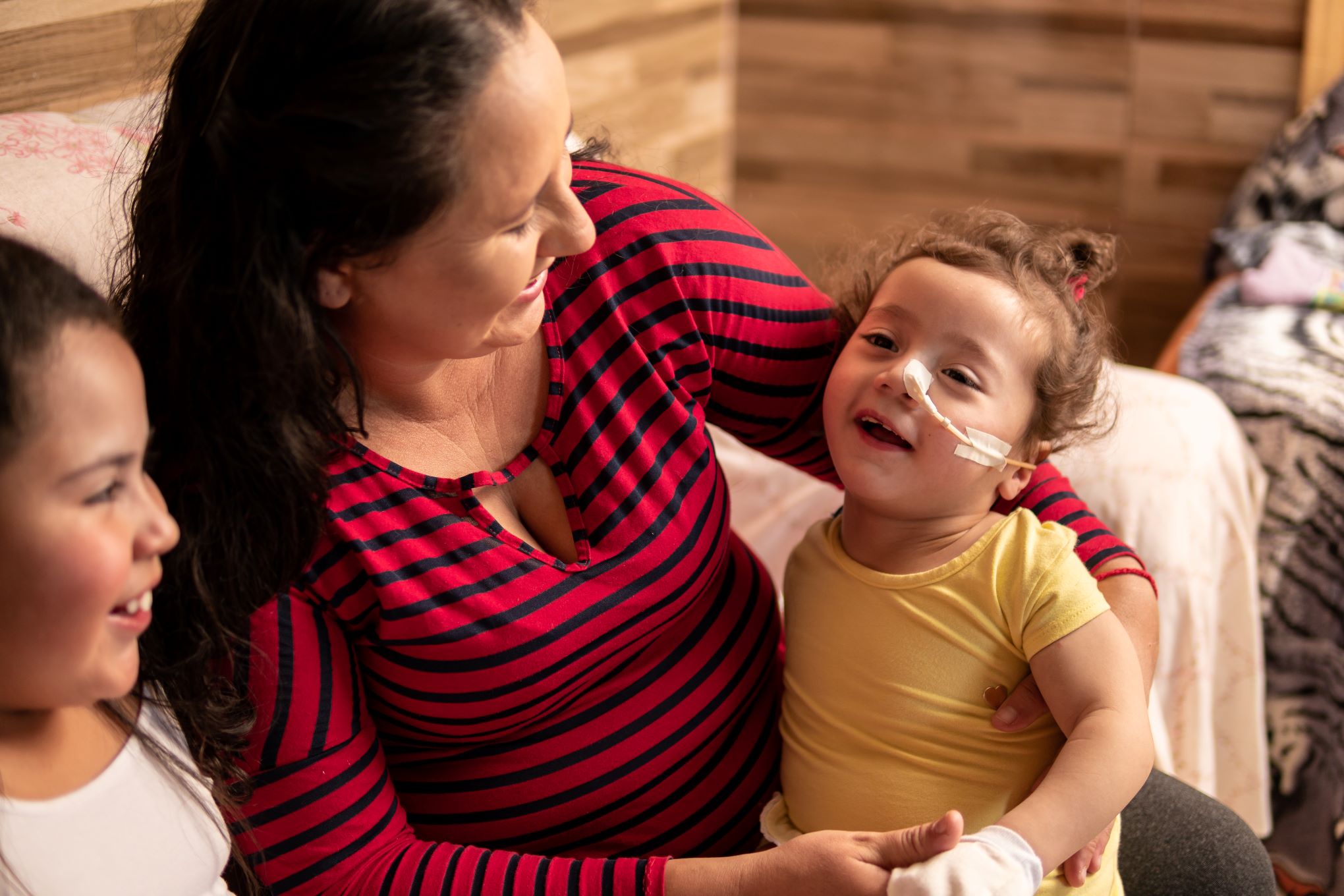 Mother with two children holds younger daughter who has a disability.
